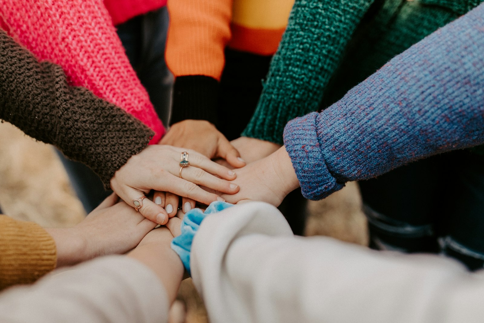 A group of people in colorful sweaters stacking their hands together