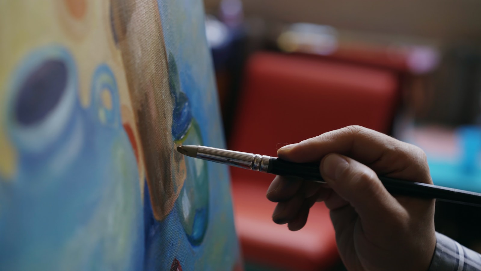 An artist&rsquo;s hand holding a brush to a canvas