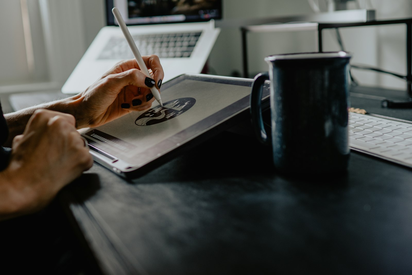 Hands sketching a logo on a drawing tablet beside a coffee mug