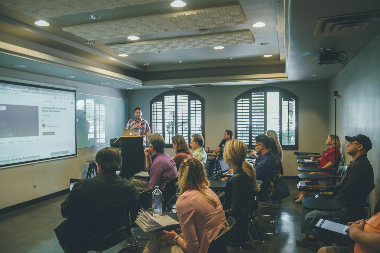 A presenter teaching a full room in front of a projector screen
