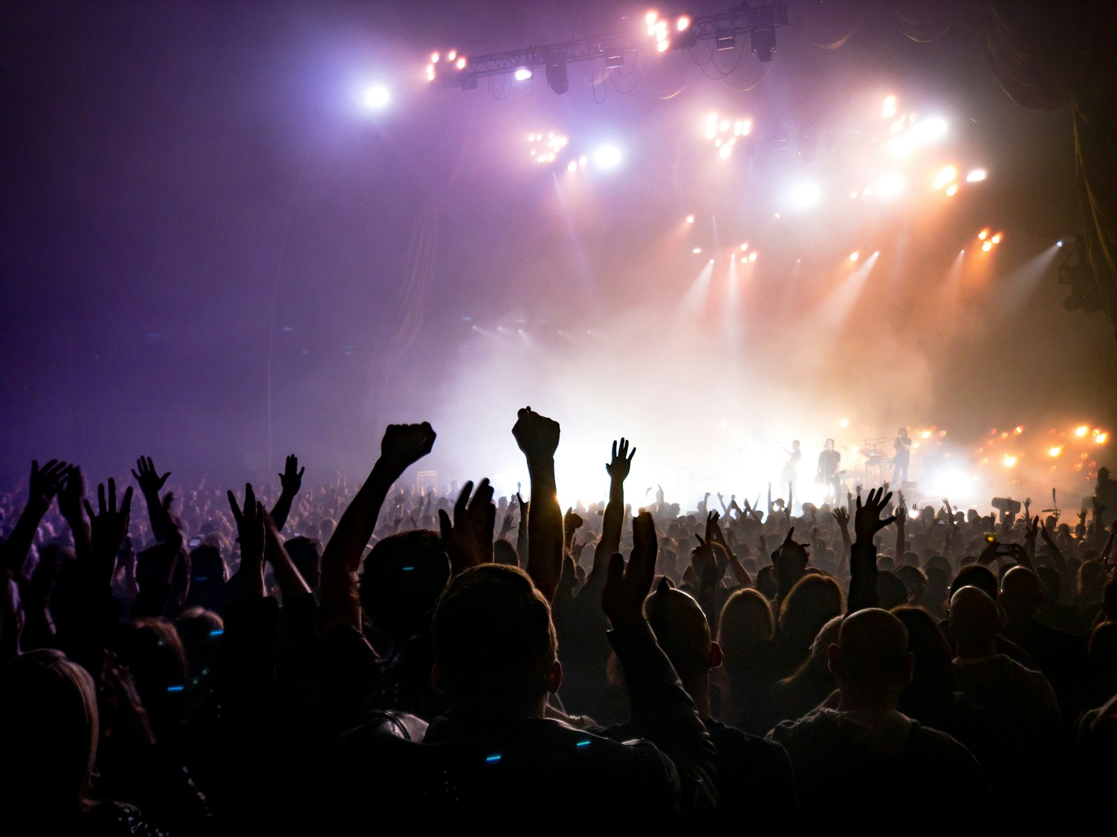 A concert crowd with raised hands facing a lit stage