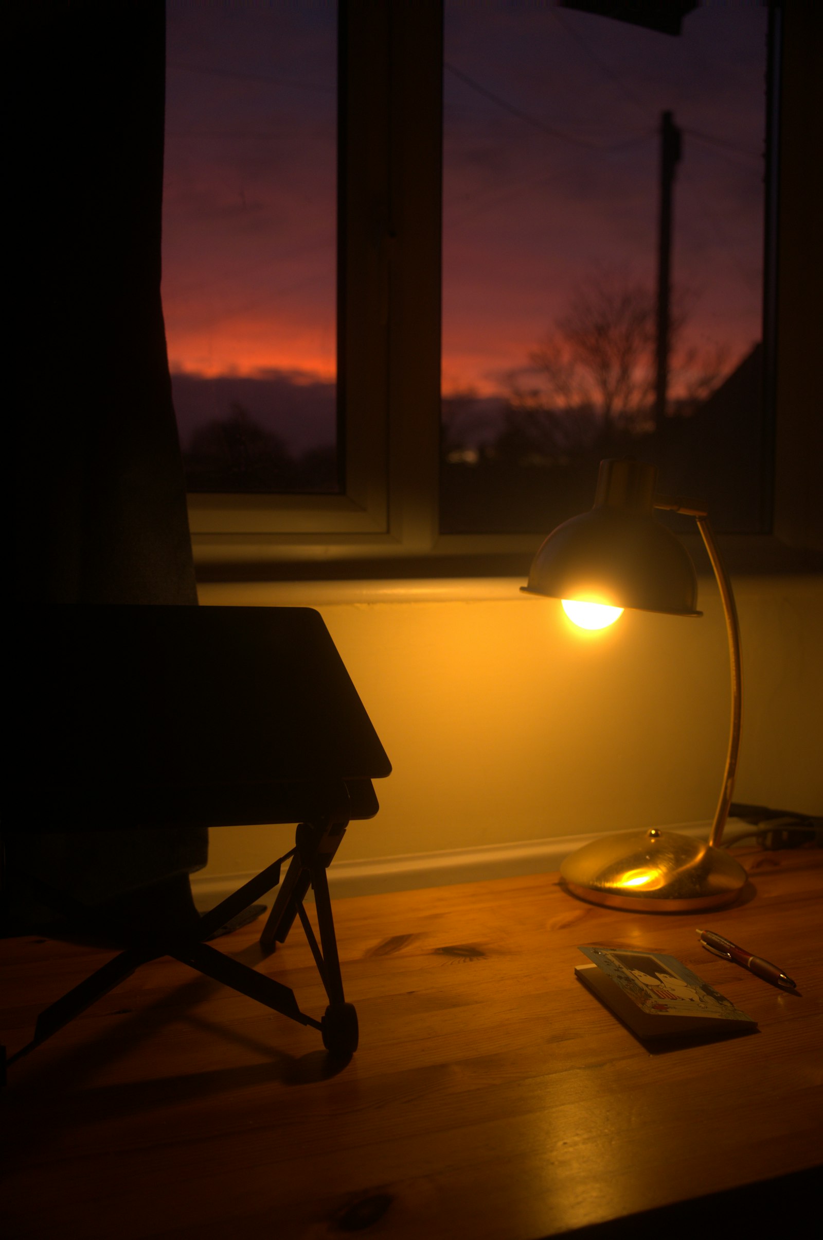 A desk lamp and notebook by a window at dusk